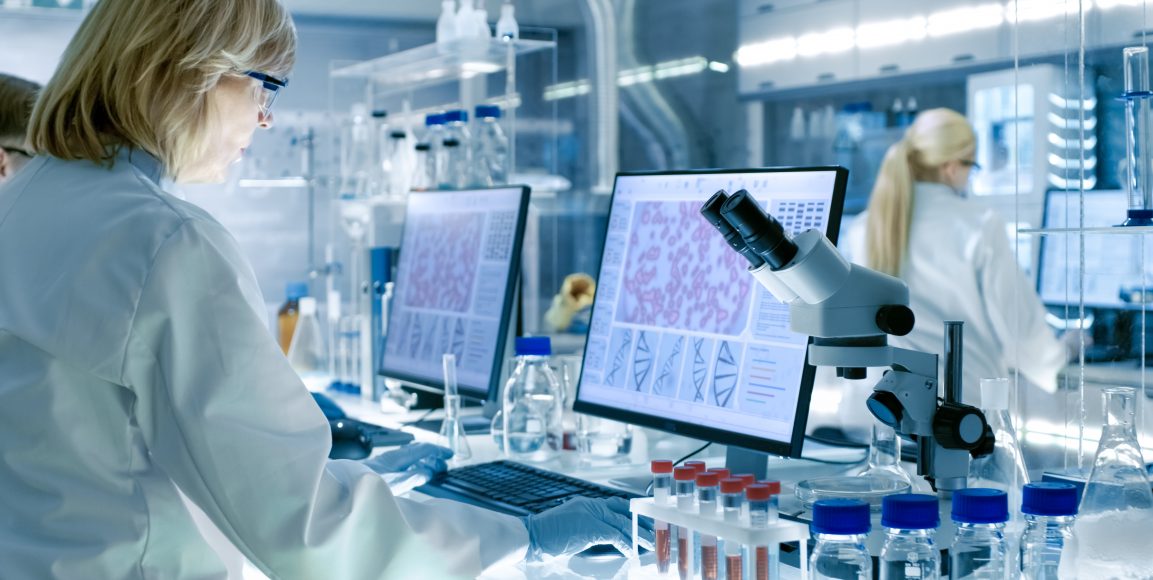 Senior Female Scientist Works with High Tech Equipment in a Modern Laboratory. Her Colleagues are Working Beside Her.